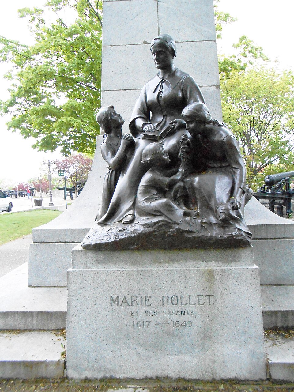 Statue en bronze de Marie Rollet assise, un livre à la main, instruisant trois enfants